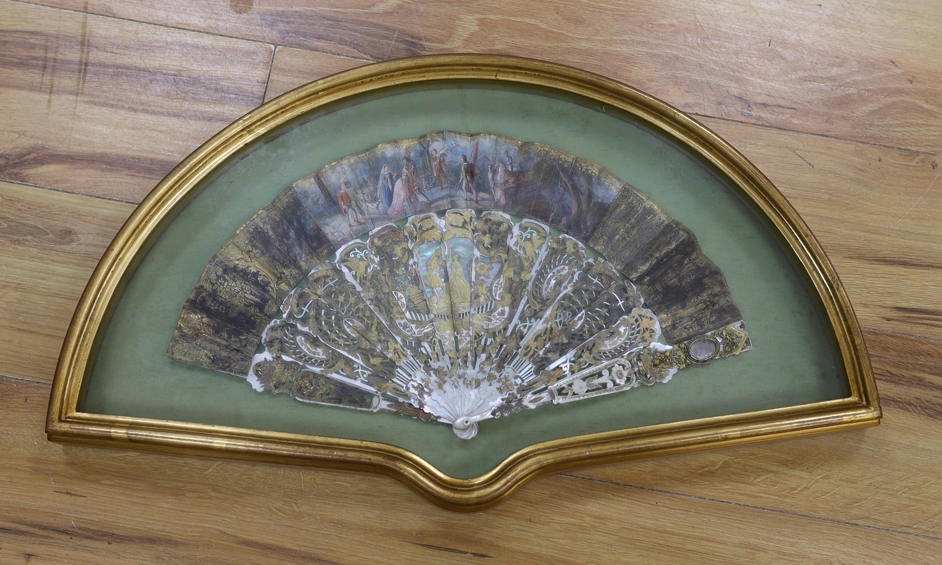 A cased early 19th century French painted paper leaf fan with gilt and mother of pearl sticks, fan 24cm high